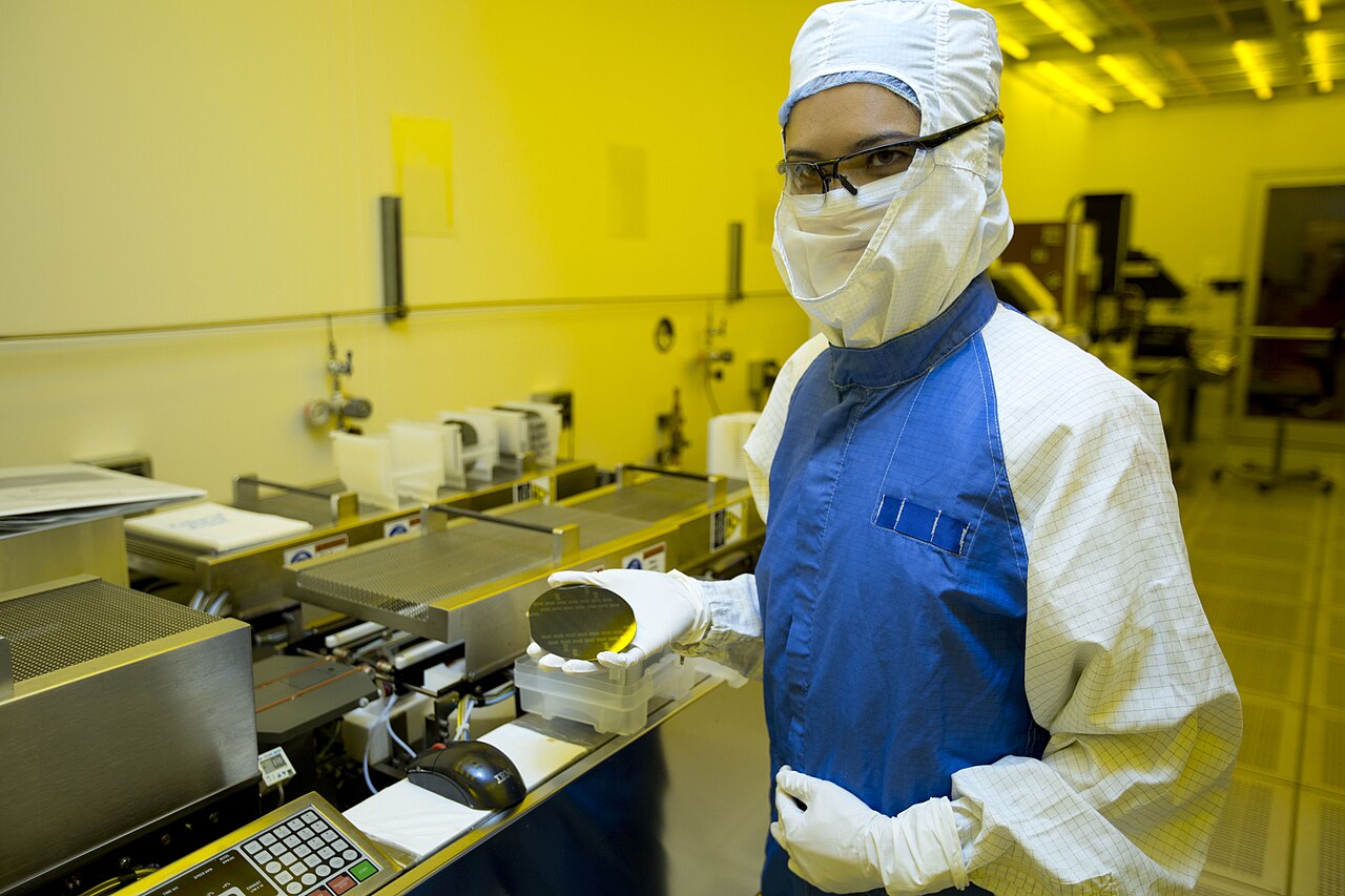 Mitarbeiterin im Reinraum hält einen Silizium-Wafer in der Hand